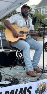 African American man sitting on stage playing acoustic guitar.