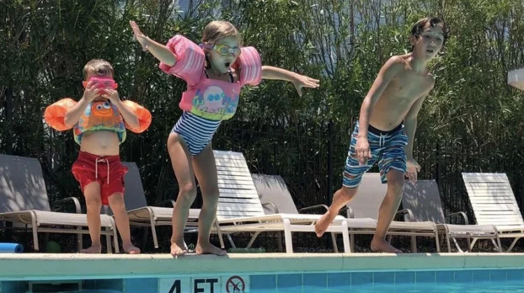 Three children energetically jumping into a pool at a vacation rental property.