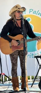 Caucasian man in casual Western attire strumming his guitar in front of an audience.