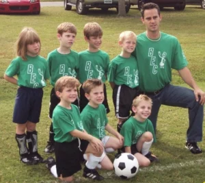 green football jersey, octagon patterned ball, coach, team members