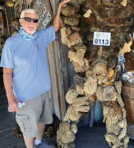 Old man posing nexr to an artistic statue made with sea coral