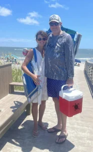 Two parents toting summer accessories while standing in the sand.