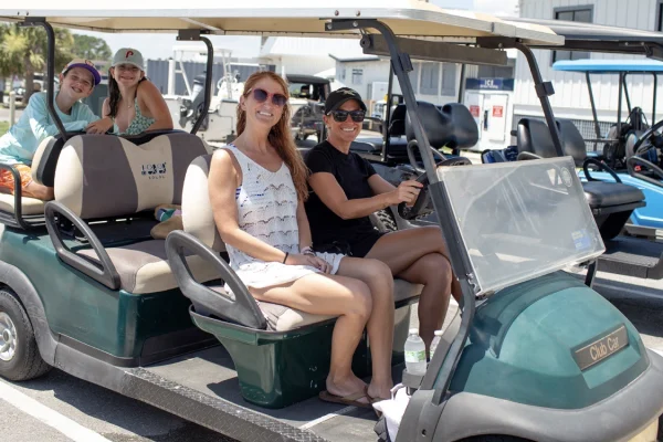 Photo of adults behind the wheel of a gold cart and two children on the rear most seat without seatbelts on.