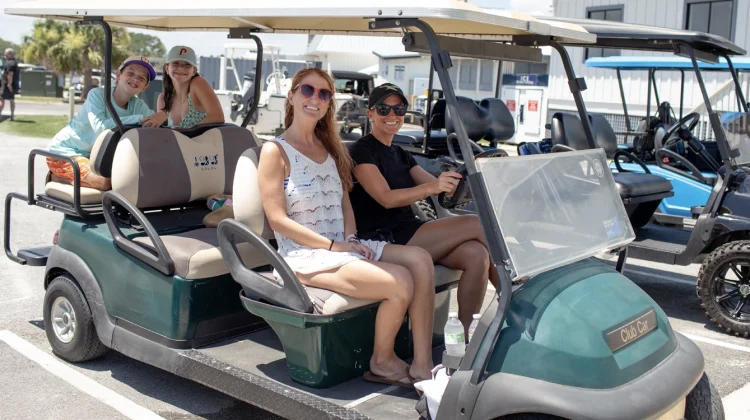 Photo of adults behind the wheel of a gold cart and two children on the rear most seat without seatbelts on.