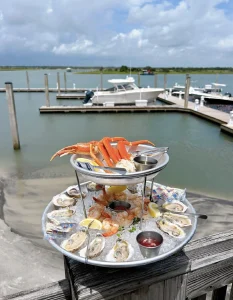 Raw oysters and crab leg appetizers on an outdoor patio banister with the Intercoastal Waterway in the background.