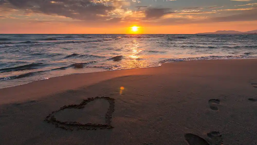 Photo of the beach with a heart and footprints for "Island couples share stories of lifelong romance". Photo by Pexels on Pixabay.com