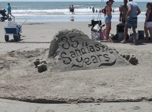 A sign in the sand acknowledging 35 years of the Sand Sculpting Competition.